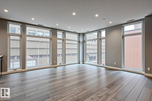 Open-concept room featuring wood-finish flooring, recessed ceiling lighting, and multiple large windows with white trim - 401 10238 103 Street, Edmonton, AB - Indoor Photo Showing Other Room