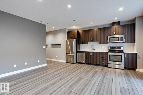 Open-concept kitchen featuring wood-grain cabinetry, stainless steel appliances, white subway tile backsplash, and light countertops - 401 10238 103 Street, Edmonton, AB - Indoor Photo Showing Kitchen With Stainless Steel Kitchen