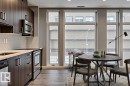 Modern kitchen and dining area featuring wood-finish flooring, dark wood-finish cabinetry, stainless steel appliances, and a light-toned tile backsplash - 401 10238 103 Street, Edmonton, AB  - Indoor 