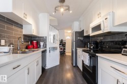 Galley kitchen featuring white cabinetry, light countertops, subway tile backsplash, stainless steel sink, and wood-finish flooring - 