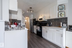 Modern kitchen featuring white cabinetry with brushed nickel hardware, light countertops, dark subway tile backsplash, and wood-finish flooring - 