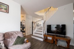 Open-concept living area featuring wood-finish flooring, a white spindle staircase with dark treads, and light-colored walls - 