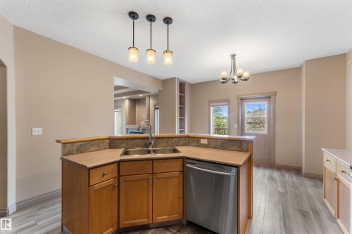 Kitchen featuring a stainless steel double sink, a built-in dishwasher, wood cabinetry, a tile backsplash, and overhead pendant lighting - 35 Oakridge Dr, St. Albert, AB - Indoor Photo Showing Kitchen With Double Sink