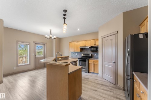 Kitchen featuring wood-finish flooring, light wood cabinetry, stainless steel appliances, and a tiled backsplash - 35 Oakridge Dr, St. Albert, AB - Indoor Photo Showing Kitchen With Double Sink