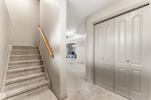 Carpeted stairway with a natural wood handrail, featuring light grey walls, white baseboards, and bi-fold closet doors with raised panels and silver-toned hardware - 35 Oakridge Dr, St. Albert, AB - Indoor Photo Showing Other Room