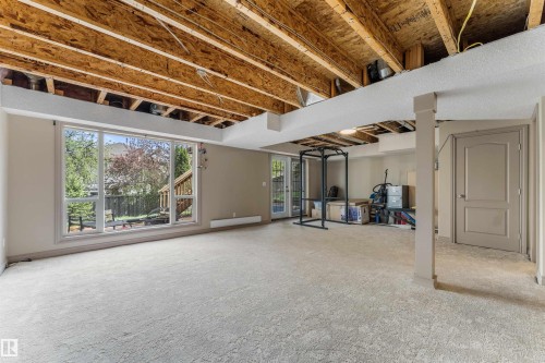 Lower level space featuring exposed ceiling joists, neutral carpeting, a large picture window, and a glass-paneled door offering exterior access - 35 Oakridge Dr, St. Albert, AB - Indoor