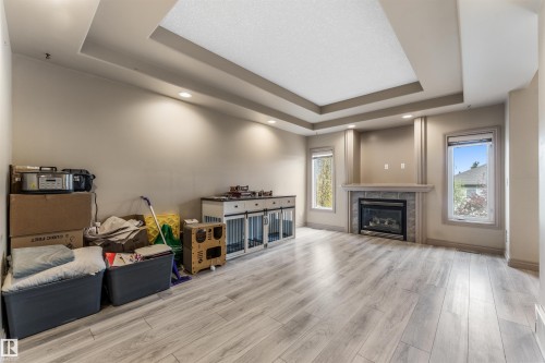 Spacious interior featuring wood-finish flooring, a tray ceiling with recessed lighting, and a fireplace with a stone surround and mantle - 35 Oakridge Dr, St. Albert, AB - Indoor Photo Showing Living Room With Fireplace