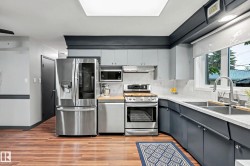 Modern kitchen featuring stainless steel appliances, light wood-finish flooring, and a large window - 