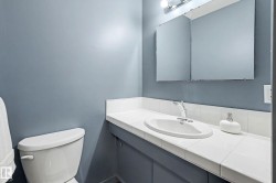 Bathroom featuring a white toilet, tile countertop, integrated sink, chrome faucet, and a medicine cabinet with integrated lighting - 