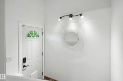 Entryway featuring a white paneled door with an arched transom window, contemporary track lighting, and a round wall mirror - 
