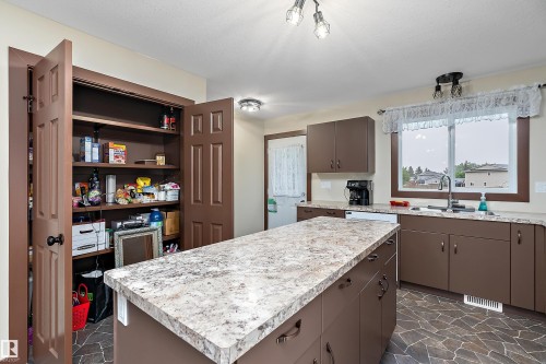 Kitchen featuring a large central island with stone-finish countertop, coordinating perimeter cabinetry, and an integrated pantry with shelving - 5210 55 Avenue, Wetaskiwin, AB 