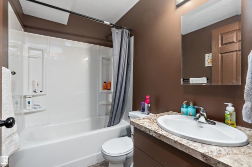 Bathroom featuring a white tub/shower combination, built-in shelving, a brown vanity with a light-toned countertop, and an oval undermount sink with chrome fixtures - 5210 55 Avenue, Wetaskiwin, AB 
