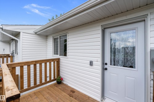 Front entryway featuring a white paneled door with a glass insert, white vinyl siding, and a wooden deck with a matching wooden railing - 5210 55 Avenue, Wetaskiwin, AB 