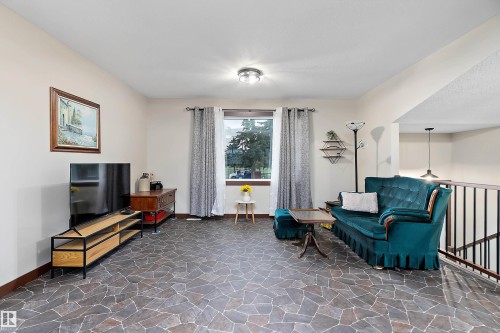 Spacious living area featuring unique flagstone-patterned flooring, a large window providing natural light, and a contemporary flush-mount ceiling light fixture - 5210 55 Avenue, Wetaskiwin, AB 