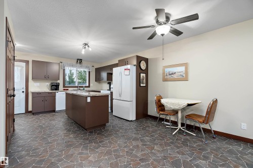 Open-concept kitchen featuring an island with a light-toned countertop, a ceiling fan with integrated lighting, and a white refrigerator - 5210 55 Avenue, Wetaskiwin, AB 