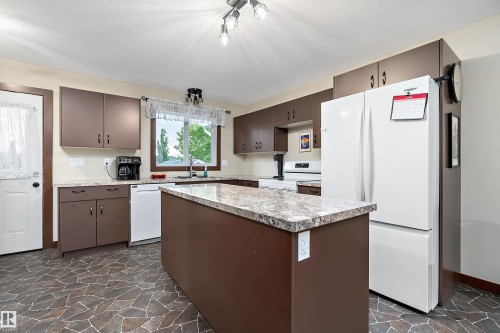 Kitchen featuring a central island with a stone-finish countertop, brown cabinetry, and patterned floor tiling - 5210 55 Avenue, Wetaskiwin, AB 