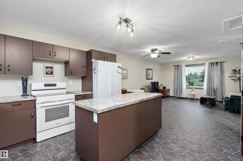 Open-concept kitchen featuring an island, brown cabinetry, and white appliances - 5210 55 Avenue, Wetaskiwin, AB 