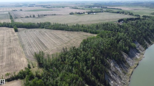 Expansive aerial perspective showcasing significant land acreage with cultivated fields and a dense tree line bordering a natural waterway - 6015 200 Street, Edmonton, AB 
