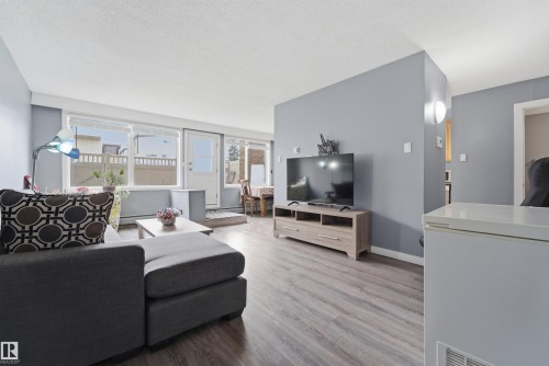 Spacious living area featuring light gray walls and wood-finish flooring - #110 7805 159 St Nw, Edmonton, AB 