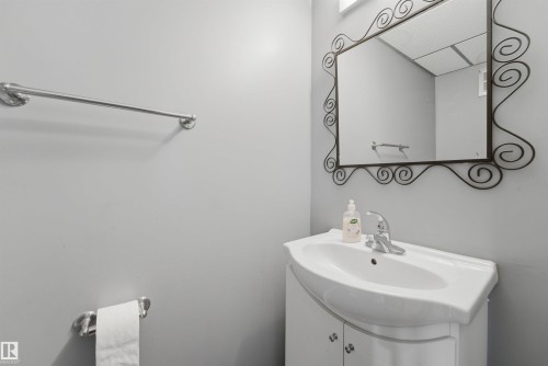 Compact bathroom vanity with integrated white basin, chrome faucet, and a decorative framed mirror - #110 7805 159 St Nw, Edmonton, AB 