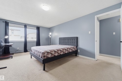 Spacious room featuring light blue walls, soft neutral carpeting, and a large window with dark drapery - #110 7805 159 St Nw, Edmonton, AB 