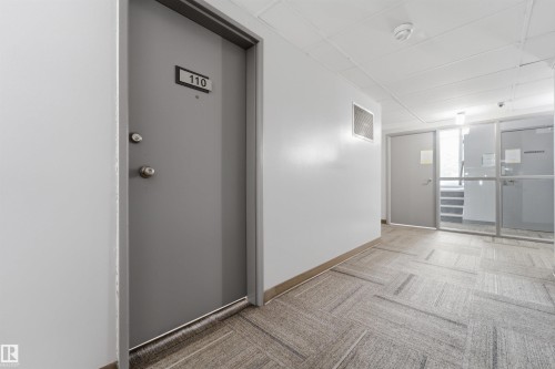 Common area hallway featuring patterned carpet flooring, white walls, and a dropped ceiling with integrated lighting - #110 7805 159 St Nw, Edmonton, AB 