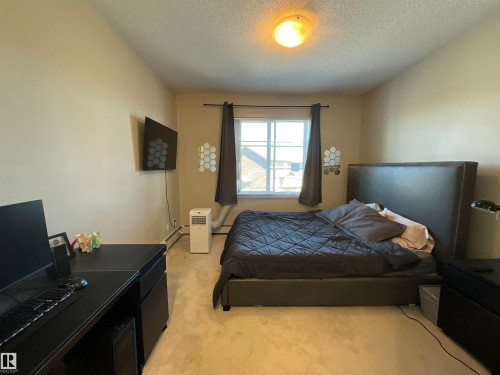Carpeted room featuring a window with dark curtains, a built-in wall-mounted television, and a ceiling light fixture - 209 1004 Rosenthal Boulevard, Edmonton, AB 