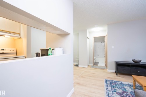 Pass-through kitchen opening to a room featuring light wood-finish flooring, light gray walls, and a recessed ceiling light - 108 2508 50 Street, Edmonton, AB 