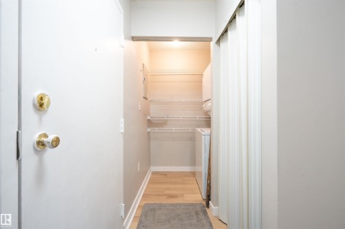 Entryway laundry area featuring wood-finish flooring, wire shelving, and a stackable washer and dryer unit - 108 2508 50 Street, Edmonton, AB 