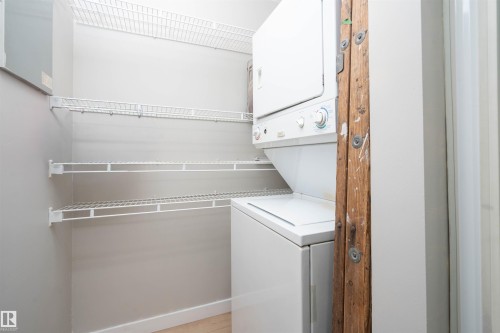 Dedicated laundry space featuring a stacked washer and dryer, multiple levels of white wire shelving, and light wood-finish flooring - 108 2508 50 Street, Edmonton, AB 