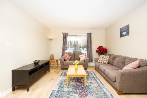 Spacious living area featuring light wood-finish flooring, neutral wall tones, and a large sliding glass door - 108 2508 50 Street, Edmonton, AB 