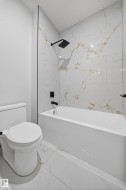 Bathroom featuring a white soaking tub, modern toilet, and large format white tiles with gold veining - 
