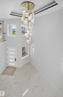 Two-story entry featuring a multi-tiered chandelier with gold accents, white porcelain tile flooring with veining, and a modern entry door with frosted glass panels - 