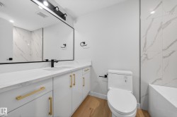 Modern bathroom featuring a long white vanity with gold-tone hardware, a rectangular undermount sink with a matte black faucet, and a large mirror with a black frame - 