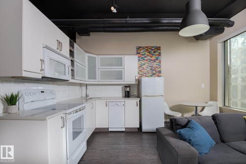 Open-concept living space featuring a full kitchen with white cabinetry, white subway tile backsplash, and light-tone countertops - 411 10024 Jasper Avenue, Edmonton, AB 