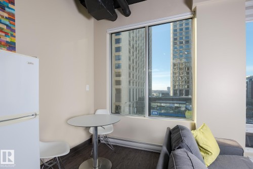 Large window with city buildings visible, dark wood-finish flooring, and light-colored walls - 411 10024 Jasper Avenue, Edmonton, AB 