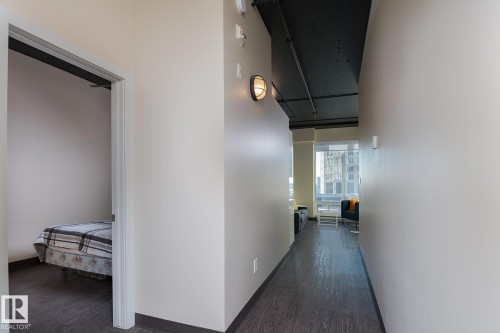 Hallway featuring wood-finish flooring, light-toned walls, and industrial-style wall sconces - 411 10024 Jasper Avenue, Edmonton, AB 