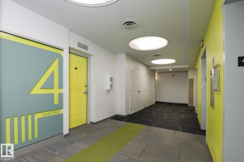 Modern hallway featuring recessed circular lighting, contrasting gray and bright yellow wall finishes, and patterned carpet flooring with a green accent strip - 411 10024 Jasper Avenue, Edmonton, AB 