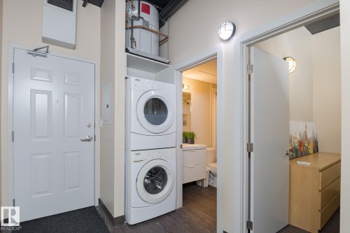Integrated laundry closet featuring a stackable washer and dryer, adjacent to a six-panel entry door - 411 10024 Jasper Avenue, Edmonton, AB 