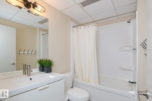 Bathroom featuring a white vanity with integrated sink, chrome faucet, and a large wall-mounted mirror - 411 10024 Jasper Avenue, Edmonton, AB 