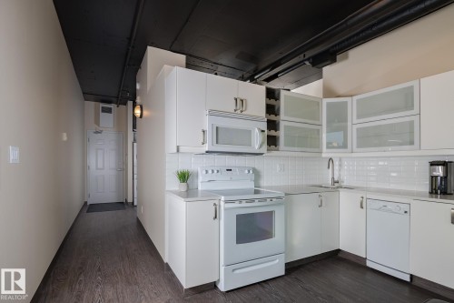Contemporary kitchen featuring white cabinetry, subway tile backsplash, and dark wood-finish flooring - 411 10024 Jasper Avenue, Edmonton, AB 
