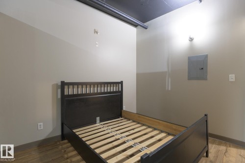 Spacious room featuring wood-finish flooring, light neutral wall paint, and exposed overhead ductwork - 412 10024 Jasper Avenue, Edmonton, AB 
