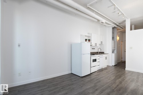Compact kitchen featuring white appliances, white cabinetry with dark hardware, and a stone-finish countertop - 910 10024 Jasper Avenue, Edmonton, AB 