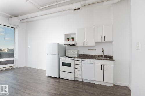 Compact kitchen area featuring white cabinetry, a dishwasher, a full-size refrigerator, and a range with overhead ventilation - 910 10024 Jasper Avenue, Edmonton, AB 