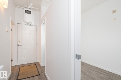Entryway featuring a paneled door with polished hardware, wood-finish flooring, and crisp white walls - 910 10024 Jasper Avenue, Edmonton, AB 