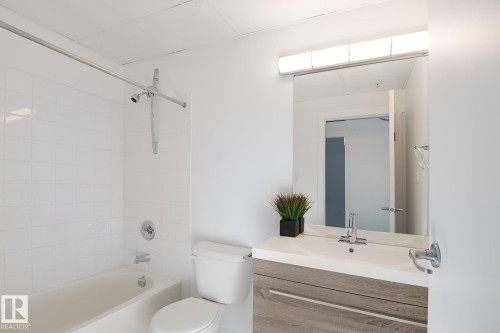 Bathroom featuring a wood-finish vanity with an integrated sink, a rectangular wall-mounted mirror, and a tub-shower combination with white subway tile surround and chrome fixtures - 910 10024 Jasper Avenue, Edmonton, AB 