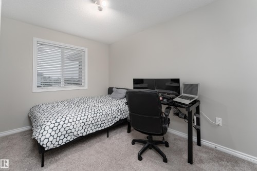 Bright bedroom featuring a single window with blinds, light gray wall paint, gray carpet flooring, and white baseboards - 9468 209 St, Edmonton, AB 