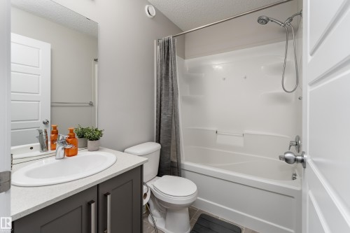 Full bathroom featuring a single vanity with a solid surface countertop, an undermount sink, a toilet, and a combined shower and bathtub with a showerhead and tub filler - 9468 209 St, Edmonton, AB 