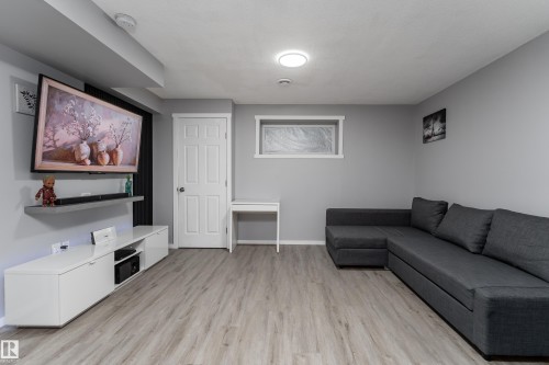 Spacious room featuring light gray walls, wood-finish flooring, a white paneled door, and a horizontal window with obscured glass - 9468 209 St, Edmonton, AB 