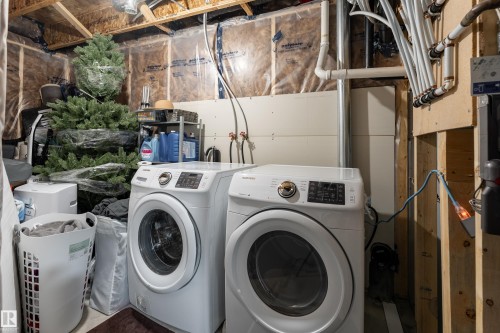 Utility area featuring a front-loading washer and dryer set, visible plumbing, and exposed wood framing - 9468 209 St, Edmonton, AB 